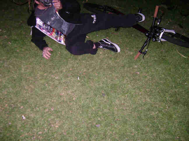 Downward, front view of a person wearing a costume, laying on grass, next to their bike at night